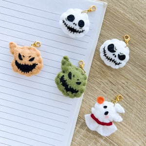 Peut inclure: Cinq porte-clés en feutre représentant des personnages d'Halloween. Les personnages sont Jack Skellington, Sally, Oogie Boogie, Zero et un fantôme. Les porte-clés sont tous blancs avec des détails noirs et sont attachés à des chaînes dorées.