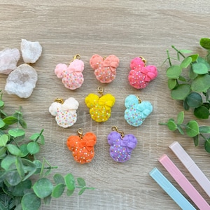 May include: Nine felt mouse head charms with a bow and sprinkles in various colors, including pink, orange, yellow, light blue, and purple. The charms are on a wooden surface.