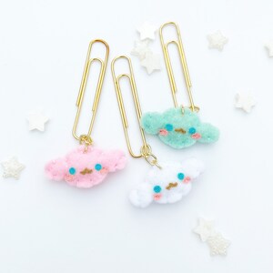 May include: Three gold paper clips with cute felt cloud charms. The clouds are pink, green, and white with embroidered eyes and mouths.