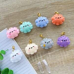 May include: A set of ten colorful felt cloud keychains with embroidered faces. Each keychain features a different color and expression, including pink, blue, green, orange, purple, and white.