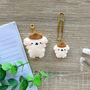 May include: Two felt dog charms with brown felt hats. The charm on the left is attached to a gold key ring. The charm on the right is attached to a gold paper clip.