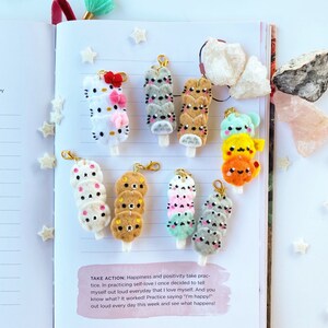 May include: A set of 8 felt keychain charms featuring different animal characters. Each charm is shaped like a popsicle and features a stack of 3-4 felt animals. The animals include a cat, a bear, a bunny, and a Hello Kitty character. The charms are attached to gold keychains.