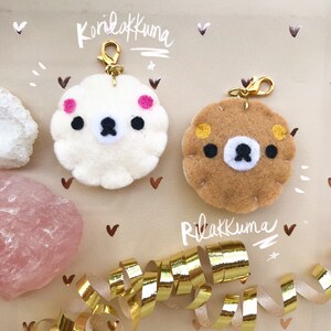 May include: Two felt keychain charms, one white with pink accents and the text "Koriakkuma" and one brown with yellow accents and the text "Rilakkuma".