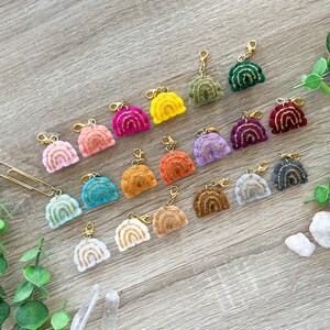 May include: A collection of 18 rainbow-shaped charms with gold glitter accents. Each charm is attached to a gold lobster clasp.