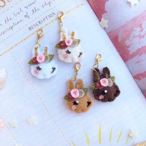 May include: Four felt bunny charms with gold glitter and floral headbands. The bunnies are white, brown, and tan. The charms are attached to gold jump rings.