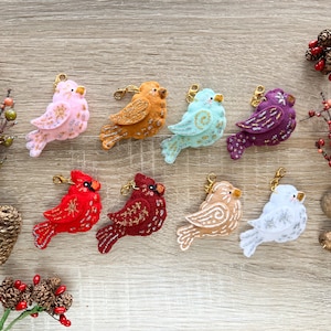 May include: A set of ten felt bird ornaments with gold, red, white, pink, purple, and blue accents. The ornaments are attached to gold keychains and are perfect for decorating a Christmas tree or adding a festive touch to a gift.