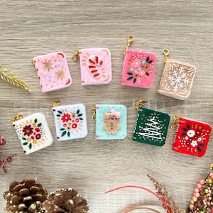 May include: Ten small felt ornaments with gold string loops. The ornaments are decorated with various Christmas themes, including snowflakes, candy canes, gingerbread people, and Christmas trees. The ornaments are arranged in a semi-circle on a light brown wooden surface.