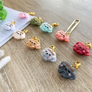 May include: A set of ten felt animal charms with gold keychains. The charms are in various colors, including pink, green, blue, brown, gray, and red. Each charm has a cute animal face with a brown stripe across its eyes.