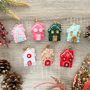 May include: Seven felt house ornaments with gold accents and embroidery details. The houses are in various colors, including pink, green, blue, white, brown, and red. Each house has a gold loop for hanging.