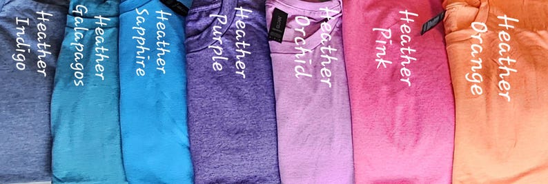 May include: A row of ten t-shirts in different colors, including indigo, teal, sapphire, purple, orchid, pink, and orange. Each shirt has the word "Heather" printed on it, followed by the color name.