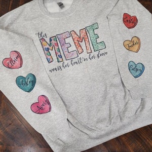 May include: Gray sweatshirt with the text "This Meme wears her heart on her sleeve" and five colorful heart-shaped patches with names on them.