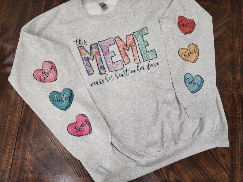 May include: Gray sweatshirt with the text "This Meme wears her heart on her sleeve" and five colorful heart-shaped patches with names on them.