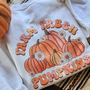 May include: White sweatshirt with a graphic design of pumpkins and the text "Farm Fresh Pumpkins" in a retro font.