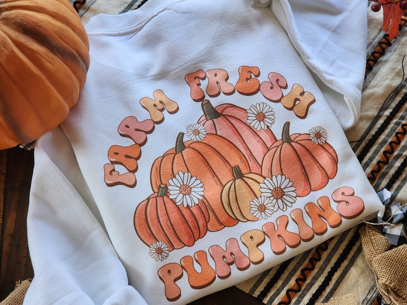 May include: White sweatshirt with a graphic design of pumpkins and the text "Farm Fresh Pumpkins" in a retro font.