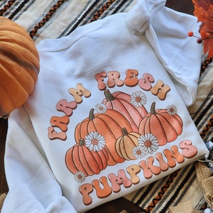 May include: White sweatshirt with a graphic design of pumpkins and the text "Farm Fresh Pumpkins" in a retro font.