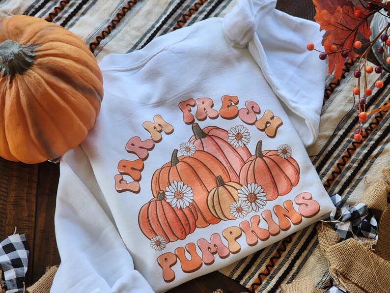 May include: White sweatshirt with a graphic design of pumpkins and the text "Farm Fresh Pumpkins" in a retro font.