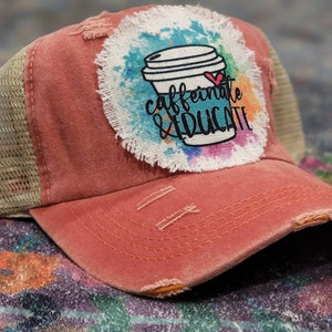 May include: A red and beige trucker hat with a distressed look. The hat has a colorful patch with a coffee cup and the text "caffeinate & educate".