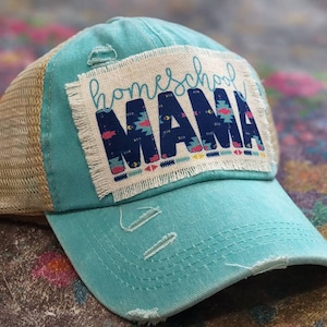 May include: A turquoise blue and beige mesh trucker hat with a distressed patch that reads "homeschool mama" in colorful letters with a geometric pattern.