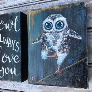 Puede incluir: Dos bloques de madera. Un bloque est&aacute; pintado de negro con una inscripci&oacute;n blanca que dice "owl always love you". El otro bloque presenta una pintura de un b&uacute;ho con grandes ojos azules, posado en una rama. El b&uacute;ho est&aacute; pintado en tonos de blanco, gris y marr&oacute;n.