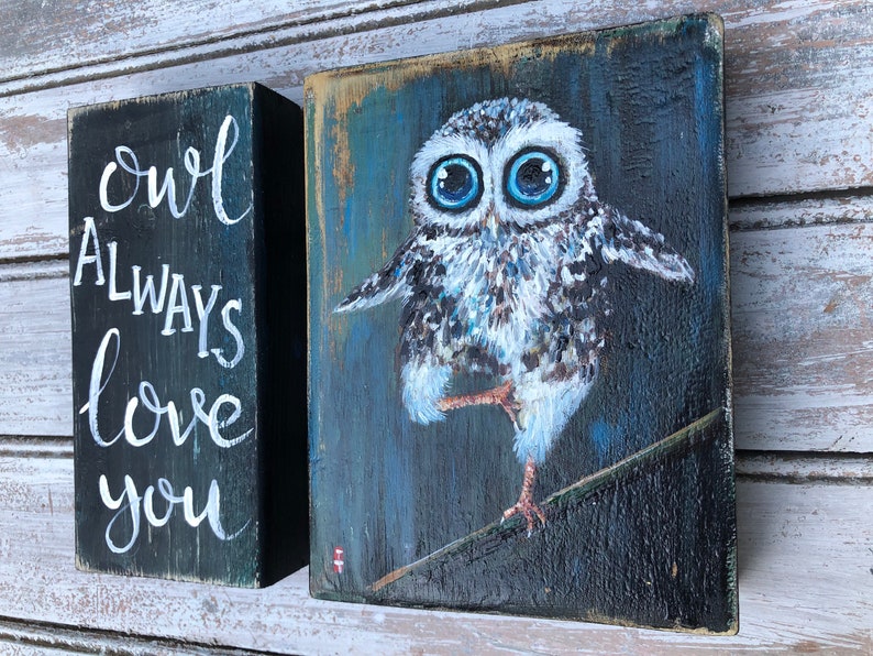 Puede incluir: Dos bloques de madera. Un bloque est&aacute; pintado de negro con una inscripci&oacute;n blanca que dice "owl always love you". El otro bloque presenta una pintura de un b&uacute;ho con grandes ojos azules, posado en una rama. El b&uacute;ho est&aacute; pintado en tonos de blanco, gris y marr&oacute;n.