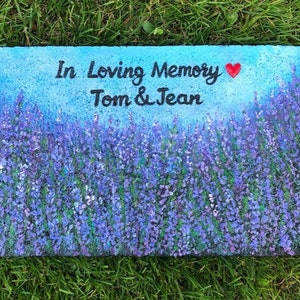May include: A painted stone memorial with a lavender field background. The stone reads "In Loving Memory Tom & Jean" with a red heart.