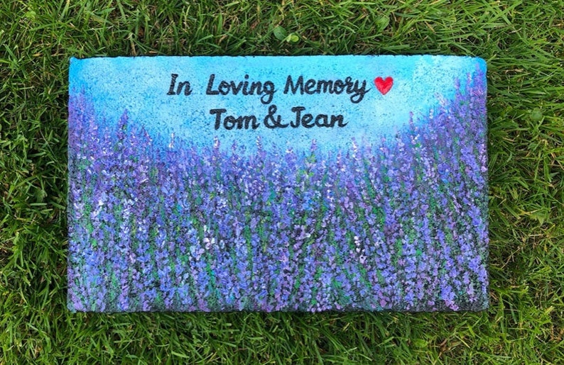 May include: A painted stone memorial with a lavender field background. The stone reads "In Loving Memory Tom & Jean" with a red heart.