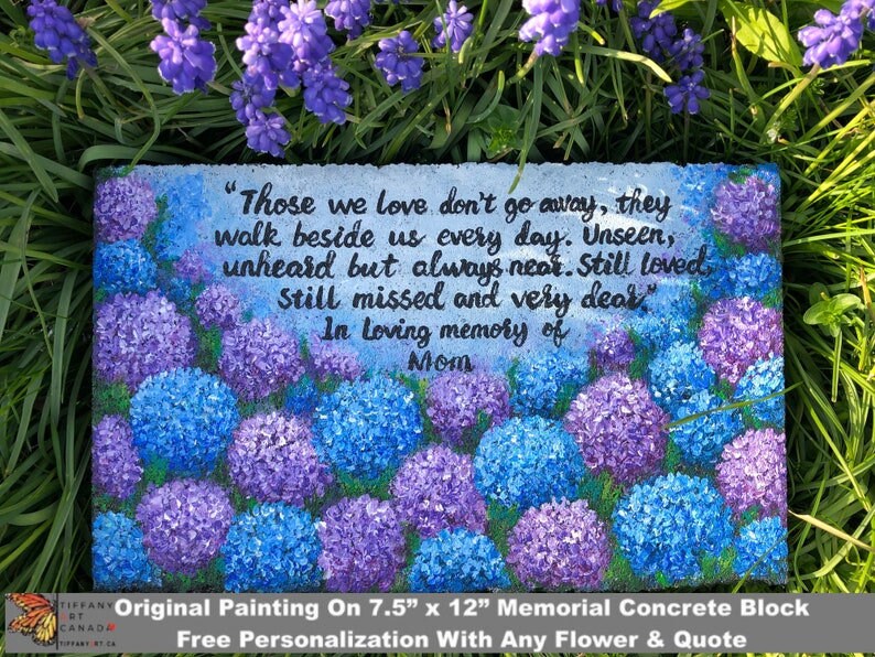 May include: A painted concrete memorial block with a quote about those we love. The block features a floral design with blue and purple hydrangeas. The quote reads "Those we love don't go away, they walk beside us every day. Unseen, unheard but always near. Still loved, still missed and very dear." The block is 7.5 inches by 12 inches.