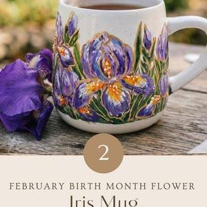 May include: A speckled white ceramic mug featuring hand-painted purple iris flowers with gold accents. The text on the image reads: 2, FEBRUARY BIRTH MONTH FLOWER, Iris Mug, HAND PAINTED WITH LOVE, PERSONALIZED GIFT - ADD YOUR CUSTOM TEXT.