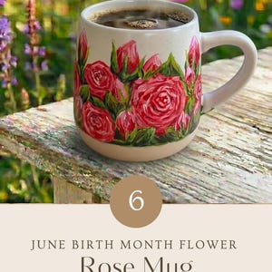 May include: A cream-colored ceramic mug featuring a hand-painted design of vibrant red roses and green leaves. The mug is filled with dark coffee and includes the text 6 JUNE BIRTH MONTH FLOWER Rose Mug HAND PAINTED WITH LOVE.