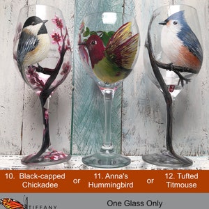 May include: Three hand-painted wine glasses featuring different birds: a Black-capped Chickadee, an Anna's Hummingbird, and a Tufted Titmouse. Each glass has a unique bird design with floral or branch accents. The text on the image says "One Glass Only, Original Painting."