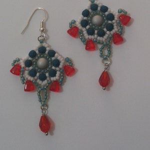 Op de afbeelding: Een paar oorhangers met een wit, blauw en rood parelmotief. De oorhangers hebben een zilveren haak en een traanvormige rode parel aan de onderkant.