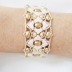 May include: A gold and white beaded bracelet with a geometric pattern. The bracelet is made with small, round beads and larger, triangular beads.