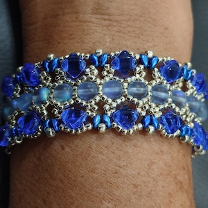 Op de afbeelding: Een kralenarmband met een zilveren en blauwe kleurstelling. De armband heeft een herhalend patroon van blauwe en zilveren kralen.