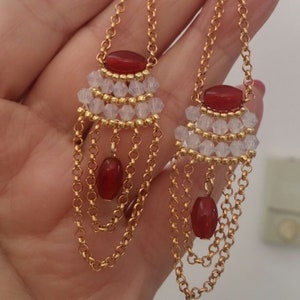 May include: A pair of long gold chain earrings with red and clear beads. The earrings have multiple layers of chain and feature a cluster of clear beads with a red bead at the top.