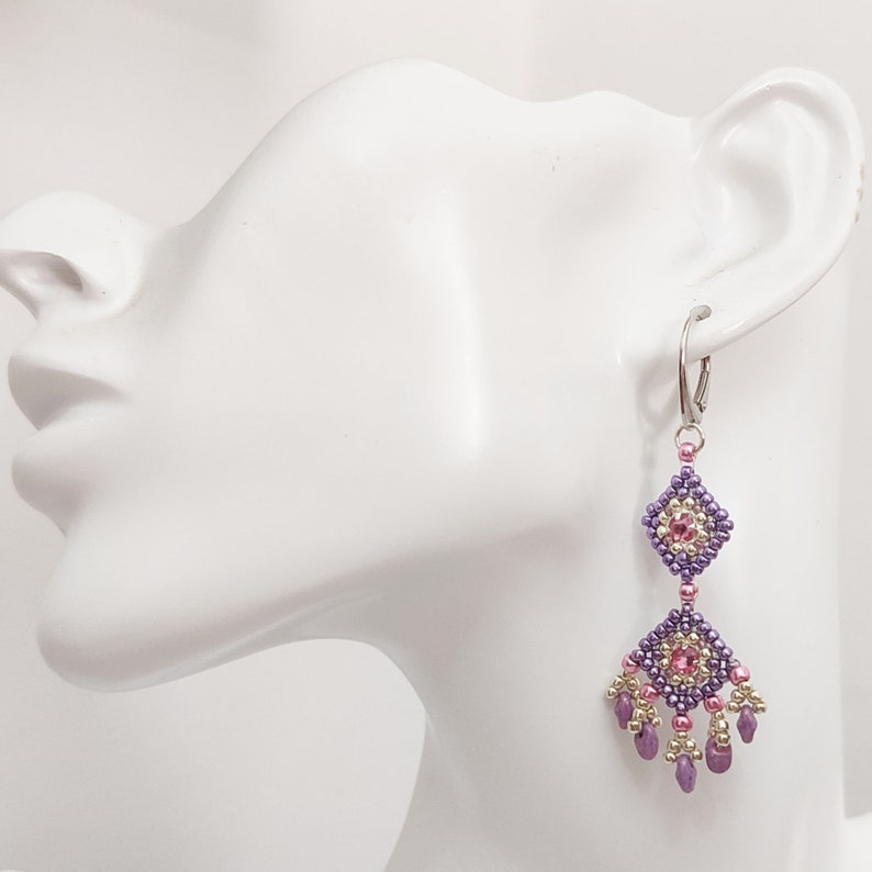K&ouml;nnte beinhalten: Lila und rosa Perlen-Ohrringe mit geometrischem Design. Die Ohrringe sind silberfarben und haben einen Hakenverschluss.
