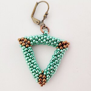 以下が含まれることがあります： 小さなビーズで作られた、ターコイズ色の三角形のデザインの手作りイヤリング。三角形の角にはブロンズ色のアクセントがあります。イヤリングにはブロンズ色のフック留めが付いています。