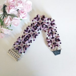 Pode incluir: Um bracelete de contas roxas e prateadas com um design de flores. O bracelete tem um fecho prateado.