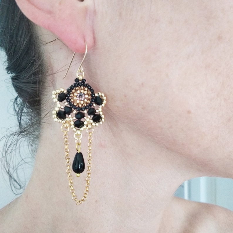 K&ouml;nnte beinhalten: Schwarze und goldene Perlenohrringe mit einer baumelnden schwarzen Perle und einer goldenen Kette.
