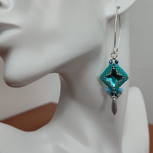 May include: Teal and silver beaded earrings with a geometric design. The earrings are dangle style and feature a teardrop-shaped pendant.
