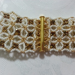 Puede incluir: Un brazalete de cuentas blancas y doradas con un cierre decorativo. El brazalete est&aacute; hecho con cuentas peque&ntilde;as y redondas y presenta un dise&ntilde;o delicado e intrincado.