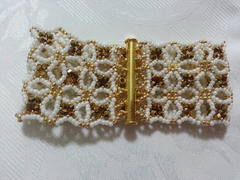 Puede incluir: Un brazalete de cuentas blancas y doradas con un cierre decorativo. El brazalete est&aacute; hecho con cuentas peque&ntilde;as y redondas y presenta un dise&ntilde;o delicado e intrincado.