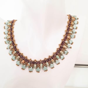 May include: A beaded necklace featuring a repeating pattern of light teal teardrop-shaped beads, dark purple faceted crystals, and small metallic bronze seed beads. The design is arranged in a symmetrical, intricate fringe-like structure.