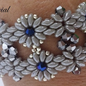 May include: A grey beaded bracelet with silver and blue accents. The bracelet is made with small, oval-shaped beads and features a repeating pattern of flower-like shapes.