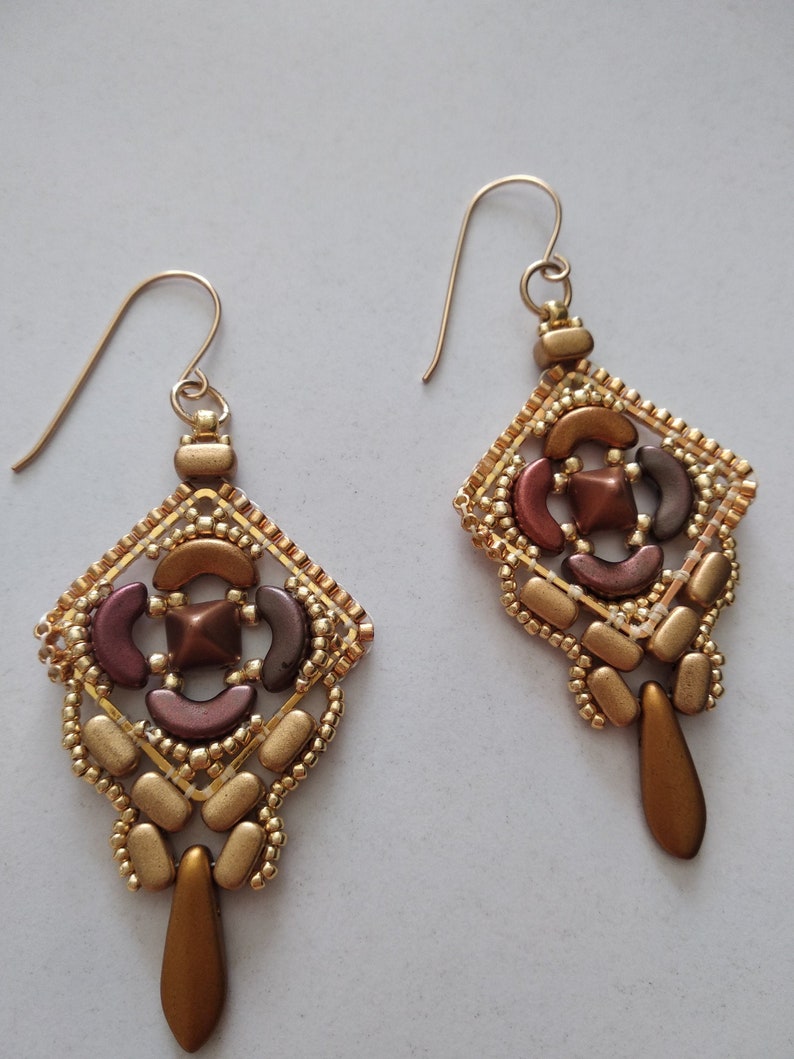 May include: A pair of gold and brown beaded earrings with a geometric design. The earrings are made with small beads and have a teardrop-shaped dangle.