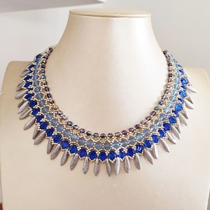 Op de afbeelding: Een blauwe en zilveren kralenketting met een aflopend ombre-ontwerp. De ketting heeft een franje van zilveren, traanvormige kralen.
