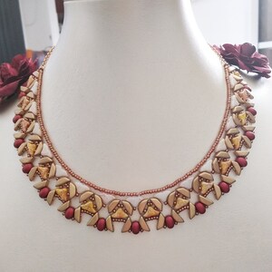 Puede incluir: Un collar de cuentas doradas y rojas con un patrón geométrico. El collar está hecho con cuentas pequeñas, triangulares y redondas.