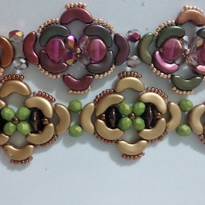 May include: A close-up of a beaded bracelet with a repeating pattern of gold, green, brown, and pink beads. The bracelet is made with small, round beads and has a delicate, intricate design.
