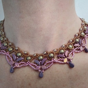 Puede incluir: Un delicado collar de cuentas con un degradado de cuentas rosas y doradas. El collar presenta un diseño floral con pequeñas cuentas en forma de lágrima que cuelgan de la parte inferior.