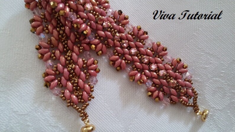 Puede incluir: Un brazalete de cuentas rosa y dorado con un dise&ntilde;o floral. El brazalete tiene dos colgantes en los extremos.