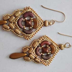 May include: A pair of gold and brown beaded earrings with a geometric design. The earrings are dangle style and have a teardrop-shaped bead at the bottom.